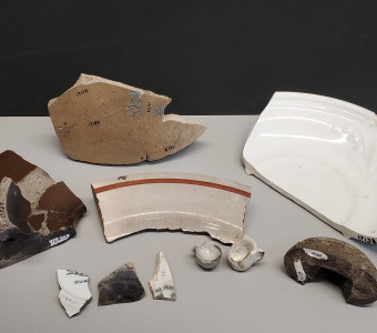 Selection of ceramics from the collection including a butter churn top, basal sherds with designs, a plate rim sherd with brown line, two toy cups, and a door knob 