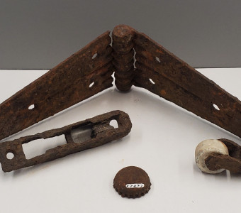 Selection of metal artifacts including a hinge, tool part, bottle cap, and roller wheel.