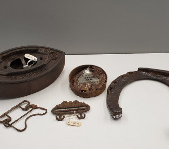 A selection of metal artifacts including a clothes iron, grape jam tin, buckles, and horseshoe, 